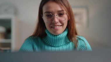 Genç ve samimi bir kadın laptopta vakit geçirip sohbet ediyor, gülümsüyor, mesajı görüyor, işe ara veriyor ve iletişimden keyif alıyor.