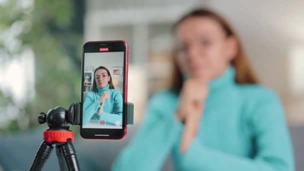 女性のブロガーのブロガーは ブロガーを通じてオンラインフォロワーと関わるために三脚に接続されたスマートフォンを使用し コンテンツを記録する時間を費やします — ストック動画