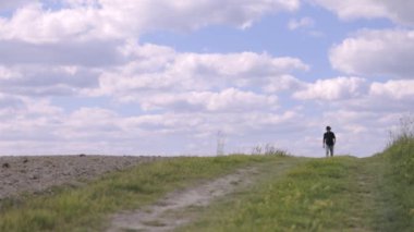 Bir adam canlı yeşil bir tepenin üzerinde yürür, yemyeşil çimlerle çevrili ve berrak bir gökyüzünün altında.