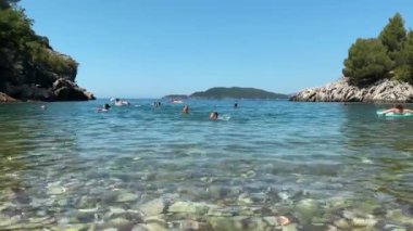 Güneşli bir günde insanlar yüzerken ve dinlenirken güzel, tenha bir koydaki berrak suyun tadını çıkar. Bu video, sakin suları ve nefes kesici havayı gösteren bu gizli taşın güzelliğini yakalıyor.