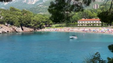 Adriyatik Denizi 'nin güzel bir sahili. Su kristal gibi berrak ve kum bembeyaz. İnsanlar güneşin tadını çıkarıyor, yüzüyor ve sahilde dinleniyorlar. Orada ağaçlar ve bir bina var.