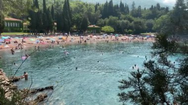 Adriyatik Denizi kıyısında güzel bir gün. Sahil manzarasının ve seslerinin tadını çıkarın. Temiz, mavi su, yemyeşil ve bol bol güneş ve suyun tadını çıkaran bir sürü insan..