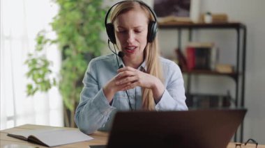 Uzaktan kumanda için modern kulaklık ve dizüstü bilgisayar kullanan, sarı saçlı becerikli bir bayan asistan. Evden destek ve çevrimiçi danışma.