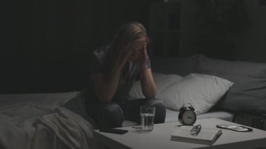 Gri pijama giymiş, yatakta oturan ve uykusuzluk çeken sinirli olgun bir kadın. Olumsuz hisleri olan beyaz bir kadın ellerini başının üstünde tutuyor..
