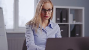 Beyaz, gözlüklü, resmi giyinmiş, iş yerinde oturan ve modern dizüstü bilgisayarda yazan olgun bir kadın. İnsan, ofis ve kariyer kavramı.