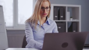 Ofis masasında otururken modern dizüstü bilgisayarla çalışan resmi giyinmiş bir iş kadını. İş sırasında meşgul görünen sarı saçlı olgun bir bayan..