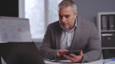 Yetişkin bir muhasebeci elinde hesap makinesiyle masada oturup dizüstü bilgisayar ekranına bakıyor. Resmi ofis çalışanı şirketin mali raporlarını kontrol ediyor..