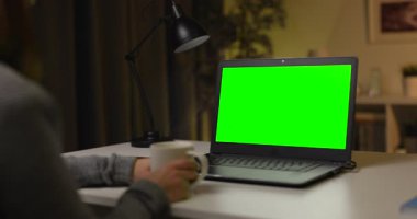 Kadın sıcak kahveyle evde oturuyor ve modern laptopta video sohbetinin tadını çıkarıyor. Akşam saatlerinde krom ekranlı taşınabilir bilgisayar kullanan bir kadın..