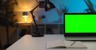 Krom ekranlı taşınabilir bilgisayar bir fincan kahve, lamba ve notlarla beyaz tablet üzerinde duruyor. Rahat dairede karanlık bir atmosfer..