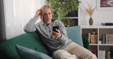 Orta yaşlı bir kadın elinde modern akıllı telefonuyla rahat bir koltukta oturuyor. Ciddi kadın hafta sonlarını evde geçirirken haber yayını yapıyor.