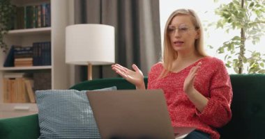 Rahat koltukta oturan ve modern dizüstü bilgisayarını video konferansı için kullanan kendinden emin olgun bir kadın. Evde uzaktan çalışma sırasında çevrimiçi toplantı.