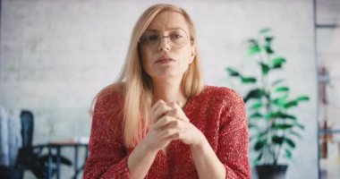 Kendine güvenen olgun bir kadının iş yerinde otururken görüntülü konuşma yapması. Beyaz kadın sarışın modern ofis geçmişiyle konuşuyor ve el kol hareketi yapıyor..