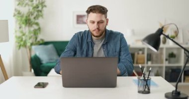 Sıradan giyinen yakışıklı bir adam ofiste oturuyor ve modern bir dizüstü bilgisayar üzerinde çalışıyor. İnsan kavramı, serbest meslek ve teknoloji.