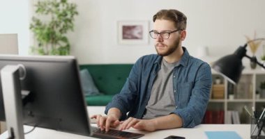 Evdeki modern bilgisayarı programlama ve kodlama için kullanan göz giysili yakışıklı bir genç. İnsan kavramı, uzaktan çalışma ve bilişim küresi.