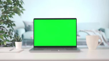 Evden dizüstü bilgisayarla çalışan bir kadın, kroma kopyalama alanı olan bir bilgisayar ekranı, bir fincan dumanı tüten kahveyle samimi bir iç mekan.