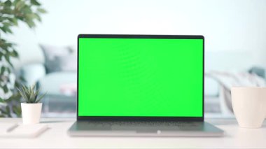 Evden dizüstü bilgisayarla çalışan bir kadın, kroma kopyalama alanı olan bir bilgisayar ekranı, bir fincan dumanı tüten kahveyle samimi bir iç mekan.