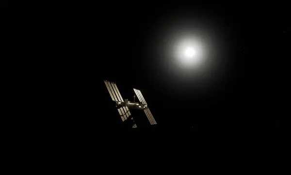 Uluslararası Uzay İstasyonu, Dünya 'nın atmosferine ve uzayına karşı siluetlendi. Arka planda güneş panelleri görünür ve parlak güneş ışığı vardı.. 