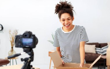 Kamerada kutuları açan genç bir kadın. Afrikalı Amerikalı kadın küçük işletme sahibi, blogger vlogger serbest çalışanı takipçileri için video içeriği kaydetmek için kamera kullanıyor