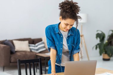 Kendine güveni tam genç Afrikalı Amerikalı kadın modern ofiste duruyor ve online laptop kullanıyor.