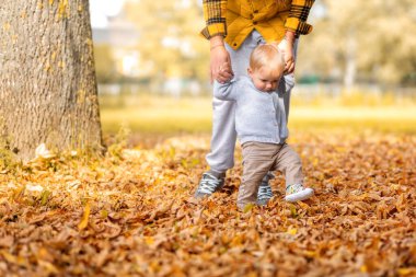 Genç bir anne çocuğuna yürümeyi öğretiyor. Küçük bebek adımları, aile zamanı konsepti