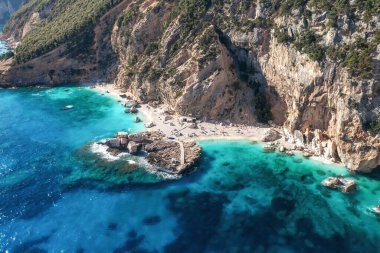 Hava manzarası taş rıhtımı ve küçük kumlu plaj manzaralı güzel bir deniz manzarası. Mavili deniz kıyısı, güneşli bir günde turkuaz berrak su, hava aracı atışı