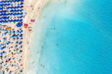 Turkuaz deniz suyu ve renkli mavi şemsiyeli güzel kumlu sahil La Pelosa manzarası, İtalya 'daki Sardunya Adaları, hava aracı çekimi.