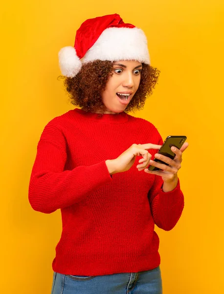 Pleasantly surprised African American woman reading message on mobile phone about big christmas sales or winning lottery standing on orange background. Good news, discounts, online shopping concept