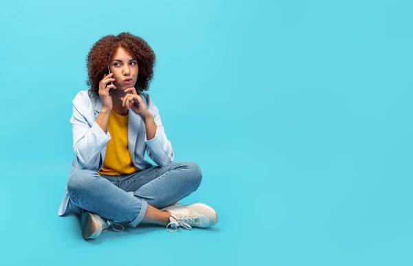 Ung Afroamerikansk Kvinna Jacka Talar Mobiltelefon Medan Sitter Blå Bakgrund Stockbild