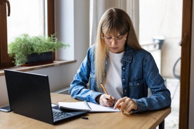 Yoğunlaşmış genç kadın evde otururken dizüstü bilgisayar kullanıyor ya da internette çalışıyor.