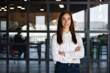Başarılı bir iş kadını, kollarını kavuşturmuş lider modern ofiste kameraya bakıyor ve gülümsüyor.