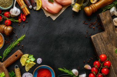 Yemek pişirmek için taze malzemelerin üst görüntüsü. Tavuklu fileto, domates, baharat, limon, sarımsak ve siyah tahta üzerine otlar.