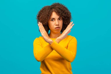 Ciddi Afrikalı genç bir Amerikalı kadın kollarını kavuşturarak X işareti yapıyor. Mavi arka planda durmaktan ya da reddedilmekten bahsediyor.