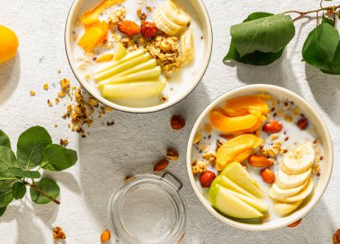 Kahvaltı kasesi gevrek granola, taze muz dilimleri, elma, kayısı ve bademle dolu. Yoğurtla kaplanmış ve besleyici bir yemek. Sağlıklı yeme kavramı