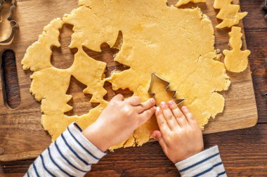 Çocuğun elleri, Noel kurabiyelerini kurabiye keskisi ve hamurla ev manzaralı tahta bir tahtanın üzerinde hazırlıyor. Sıcak tatil pişirme anı