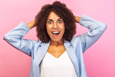 Heyecanlı kıvırcık saçlı, mavi ceketli, pembe arka planda parlak bir gülümsemeyle sürpriz yapan genç Afrikalı Amerikalı kadın. Duygular ve enerji kavramı