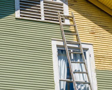 Ladder leaning against an historic house with one side freshly painted (green) and the other side not (yellow) clipart