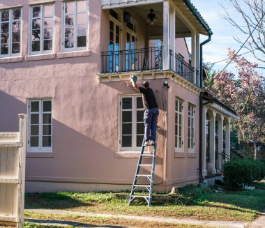 NEW ORLEANS, LA, USA - DECEMBER 9, 2022: Worker on a ladder painting the side of a pink house in the Carrollton Neighborhood