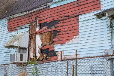 Side view of old home featuring two layers of severely damaged and rotting siding, both wood and vinyl clipart