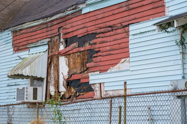 Side view of old home featuring two layers of severely damaged and rotting siding, both wood and vinyl