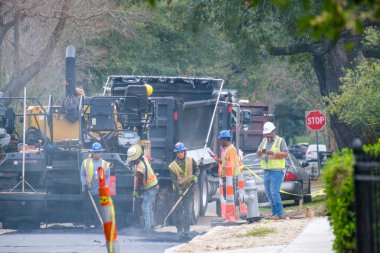 NEW ORLEANS, LA, ABD - 20 Şubat 2023: İşçiler, Uptown Mahallesi 'ndeki sokak onarım projesi sırasında ağır ekipmanların arkasındaki yol yüzeyinde sıcak, sigara içen asfalt yayıldı 