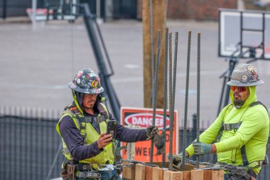 NEW ORLEANS, LA, ABD - 27 ARALIK 2023: Loyola Üniversitesi Kampüsü 'ndeki inşaat sahasında inşaat demirleri döşeyen koruyucu ekipmanlı iki inşaat işçisi