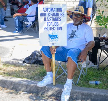 NEW ORLEANS, LA, ABD - 2 Ekim 2024: Uluslararası Liman İşçileri Derneği 'nden grev rıhtım işçisi, New Orleans Limanı girişindeki kaldırımda elinde pankartla oturuyor