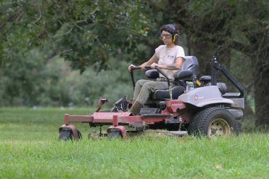 NEW ORLEANS, LA, ABD - 24 Eylül 2024: Koruyucu kıyafet giyen genç bir kadının seçici odak noktası Audubon Park 'ta Lazer E-Serisi Ekspres çim biçme makinesiyle çimleri kesmesi