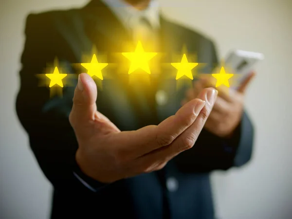 Hand of businessman giving five stars for his full satisfation. Providing a five star rating. Service rating and customer, client, business evaluation concept.