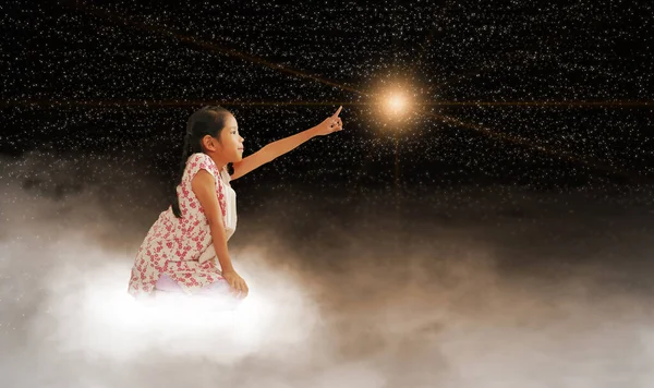 A girl reaching for the star, sitting on a cloud in dark sky, night time. Concepts of fulfilling your dream, wish, goal, and doing the impossible.