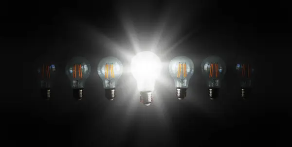 暗い背景の他の明るい電球の間で照らされたまたは輝く電球は新しい考え 創造性 知識およびインスピレーションを表します — ストック写真