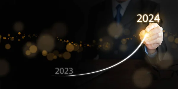 A businessman draws rising curve on virtual tech screen, from the end of 2023 rises to the start of 2024. Happy new year and welcome new business goals and  visions