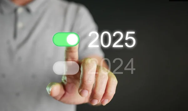 Happy new year 2025. A man tapping on an on-switch of 2025 toggle button to start and welcome the new coming year.