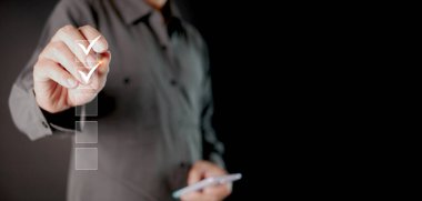 Kontrol listesi konsepti. Stylus 'u olan bir adam kutucuklardaki dijital doğru işaretleri kontrol ediyor. Akıllı performans izleme, çevrimiçi anket doldurma, karanlık arka planda akıllı telefon e-form kontrol listesi.