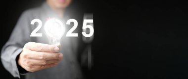 2025 fikir ve amaç. Bir adam, önümüzdeki yıl iş, teknoloji veya özel hayat için hedef ve stratejik planı temsil eden sanal dart ikonuyla aydınlatma ampulünü elinde tutuyor.